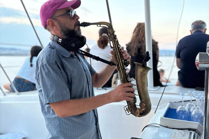 Man playing saxophone on a boat near DJ equipment.